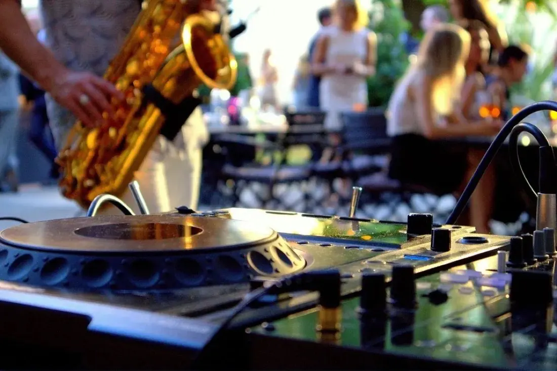 DJ-set met een saxofonist op een terras, met gasten op de achtergrond