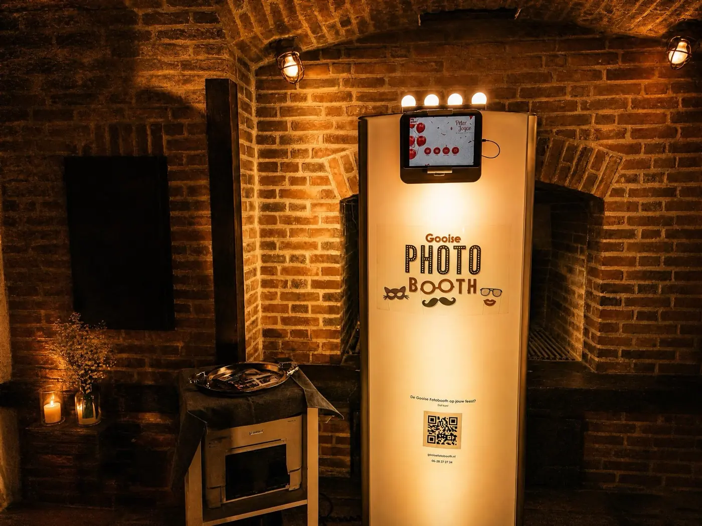 De Gooise Photobooth in warm kaarslicht in een van de oude bakstenen kalkovens van De Kalkovens in Huizen, met de printer en een dienblad vol kaarten ernaast