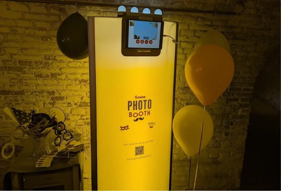 De Gooise Fotobooth met warm oranje licht, ballonnen en props bij een bakstenen muur